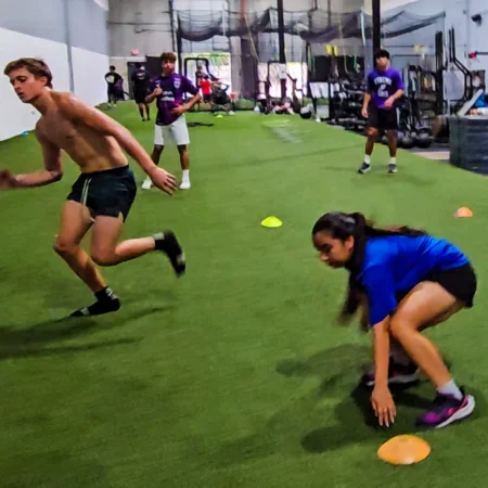 4 teens performing agility drills inside an athletic gym with turf.