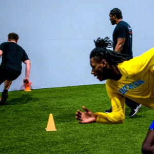 Two young men sprinting around cones while their coach watches.