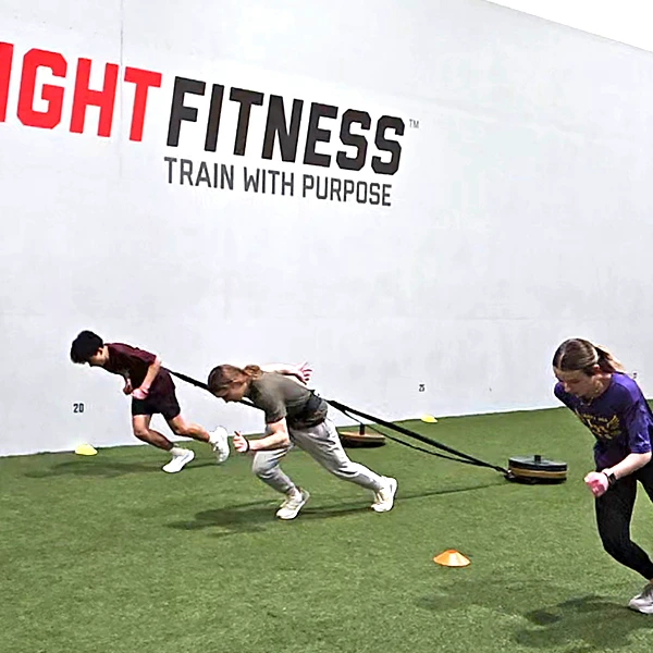 Teen athletes sprinting with a mini sled inside of an athletic training facility.