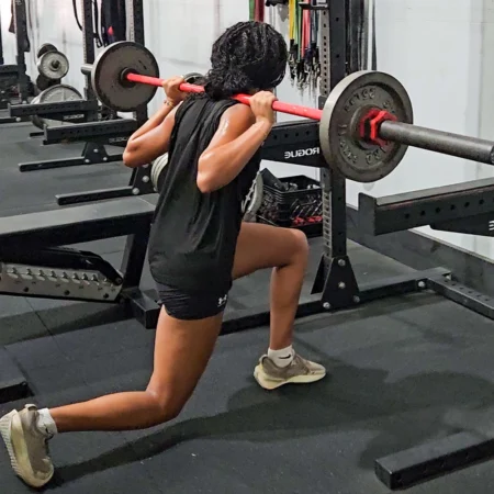 A female athlete performing barbell split squats.