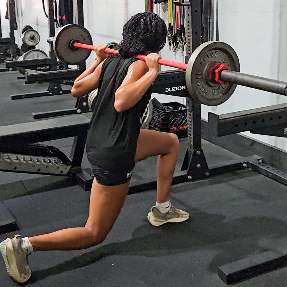 A female athlete performing barbell split squats.
